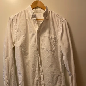 Asket skjorta  - Säljer en klassisk vit skjorta i bomull med lång ärm och knappar hela vägen ner. Perfekt för både vardag och festliga tillfällen. Skjortan har en bröstficka och en stilren design som passar till allt. 