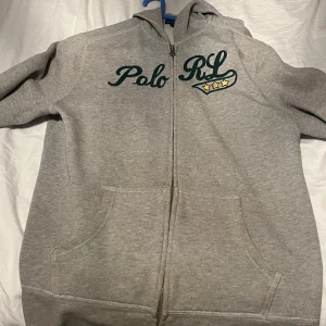 Grå hoodie från Polo RL - Säljer en grå hoodie från Polo RL i bra skick. Den har en dragkedja framtill och en snygg broderad logga med stjärnor på bröstet. Perfekt för höst och vår, och den är superbekväm att ha på sig. Passar både till vardags och chillkvällar. 🧢