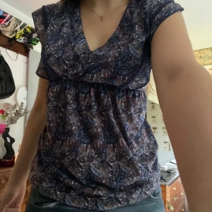 Mönstrad blus med v-ringning - Säljer en snygg blus med ett unikt mönster i blå och lila toner. Använt fåtal gånger men är köpt second hand 💕