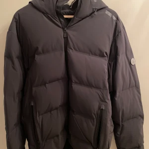 Svart dunjacka från Sail Racing - Säljer en svart dunjacka från Sail Racing i storlek medium. Jackan har en stilren design med dragkedja och två praktiska fickor framtill. Perfekt för kalla dagar med sin varma och bekväma passform. Den har en diskret logga på ärmen och är i mycket bra skick.