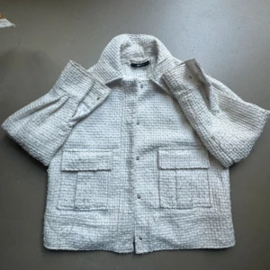 Vit jacka från Gina Tricot - Säljer en superfin vit jacka från Gina Tricot i storlek S. Den har en texturerad yta med två stora fickor framtill och knappar. Perfekt för en stilren look i vår och sommar! 🕊️