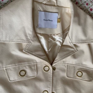 House of Sunny trenchcoat i veganskt läder med gulddetaljer - Chic trenchcoat med bälte i veganskt läder från House of Sunny🎀jackan är i bra skick men har tecken på användning som kan ses i bilderna, stygnen på lappen har även lossnat🫶storlek 34, passar även storlek 36