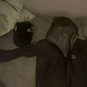 Svart vindjacka från Haglöfs - Säljer en svart vindjacka från Haglöfs i bra skick. Jackan har en praktisk huva och dragkedja framtill. Perfekt för höst och vår, med en stilren design och bekväm passform. Den har också två fickor med dragkedjor för säker förvaring. Passar både för vardag och lättare friluftsaktiviteter.