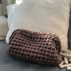 Brun virkad väska - Säljer en superfin brun virkad väska som är perfekt för hösten. Den är handgjord med ett grovt stickat mönster och har en mysig känsla. Perfekt för att bära småsaker eller som en dekorativ detalj i hemmet. Väskan är i mycket bra skick och redo för en ny ägare!