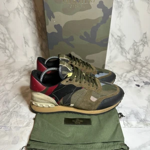 Valentino rockrunner - Säljer ett par snygga Valentino Rockrunner sneakers i camouflage. Skorna har en cool mix av gröna, röda och beige toner stl 39 men passar 40 med mocka- och skinnmaterial. De har snörning och en unik nitar-detalj på hälen. Perfekta för en trendig look!