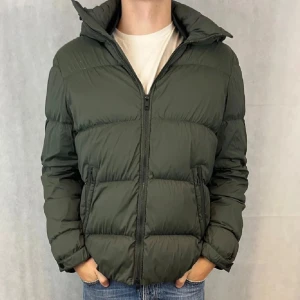 J Lindberg Jacka  - Säljer en snygg grön pufferjacka med huva från J Lindberg, perfekt för kalla dagar. Riktigt nice J Lindberg  jacka i storlek L. Passar även M. Väldigt fint skick. Modellen är 185.