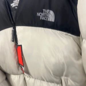 Grå och svart dunjacka från The North Face - Säljer en stilren grå och svart dunjacka från The North Face. Jackan har en dragkedja framtill och är perfekt för kyligare väder. Den har en klassisk design med logotypen på bröstet. Priset kan diskuteras och det finns många storlekar av denna jacka