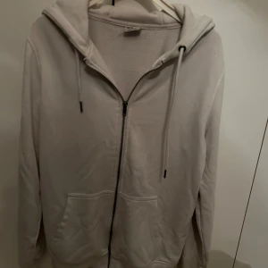 Vit hoodie från Urban Classics - Säljer en stilren vit hoodie från Urban Classics i storlek S. Den har en dragkedja framtill och praktiska fickor. Perfekt för en avslappnad look.