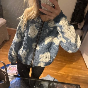 Blå och vit quiltad bomberjacka - Säljer en cool blå och vit quiltad bomberjacka med dragkedja. Jackan har ett unikt mönster och långa ärmar. Perfekt för att ge din outfit en extra edge.