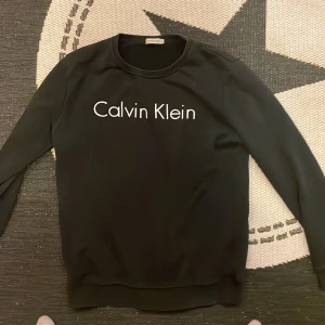 Svart tröja från Calvin Klein - Säljer en stilren svart tröja från Calvin Klein med deras ikoniska logga på bröstet. Tröjan har långa ärmar och en rund halsringning. Perfekt för en avslappnad look.