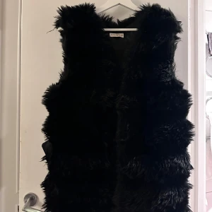 Svart pälsväst från Giorgia - Snygg svart pälsväst från Giorgia, perfekt för att hålla sig varm och stilren. Västen har en mjuk och fluffig textur som ger en lyxig känsla. Passar utmärkt för kyligare dagar.