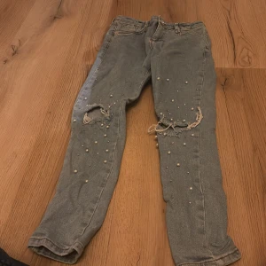 Blå jeans med pärlor från River Island - Snygga blå jeans från River Island med coola slitningar och pärldetaljer på framsidan. Perfekta för en trendig look med en touch av edge. Passar bra för barn i åldern 10 år.