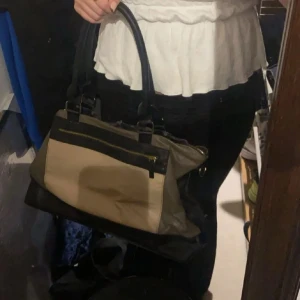 Beige och svart handväska - Snygg handväska i beige och svart med dragkedja. Perfekt för att bära dina dagliga nödvändigheter med stil. Den har en praktisk storlek och bekväma handtag.