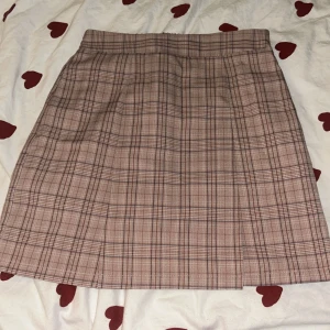 Rutig kjol i rosa - Snygg rutig kjol i rosa med en klassisk design. Kjolen har två små slits framtill och elastisk midja baktill för extra komfort. Perfekt för en stilren look. Priset kan sänkas mycket vid snabb affär 😊