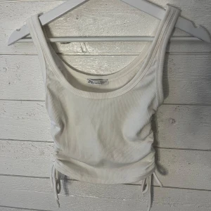 Vit ribbad linnetopp - Säljer en vit ribbad linnetopp från Zara. Toppen har en croppad design med knytbara detaljer på sidorna för en justerbar passform. Perfekt för varma dagar!