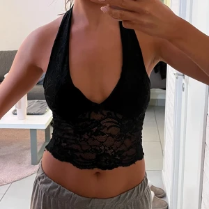 Svart spetslinne - Snyggt svart spetslinne med halterneck och djup urringning. Toppen är croppad och har ett vackert spetsmönster som ger en elegant touch. Perfekt för en kväll ute eller en speciell tillställning.