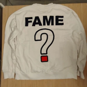 Vit sweatshirt från Piazza Italia - Säljer en vit sweatshirt från Piazza Italia med texten 'FAME' och ett stort frågetecken på baksidan. Framsidan har ett rött frågetecken på bröstet. Perfekt för en avslappnad stil.