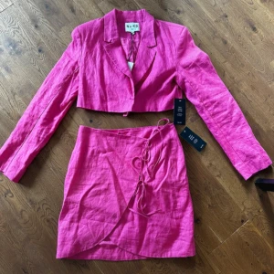 Rosa set med omlottkjol och kavaj från NA-KD  - Trendig rosa omlottkjol från NA-KD i linne. Kjolen har en knytning i sidan och en kort design som passar perfekt för varmare dagar. Även en kort kavaj till. 