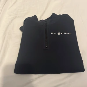 Svart halt zip tröja från Sail Racing - Snygg mörk blå half zip  tröja från Sail Racing med dragkedja och logga på bröstet. Perfekt för en stilren och sportig look. Tröjan har långa ärmar och är tillverkad i ett bekvämt material. Använd  max 2 gånger pga växte ut den snabbt. 