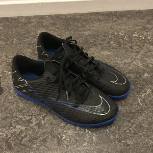 Svarta och blå Nike fotbollsskor - Snygga svarta fotbollsskor från Nike med blå detaljer och vit logga. Skorna har snörning och en smidig design för optimal prestation på planen. 🏴🏴 Det är äkta också beställd från nike webbsidan.