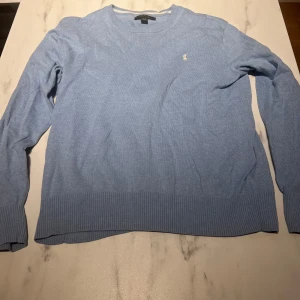  Ralph Lauren tröja - Säljer en stilren ljusblå tröja från Ralph Lauren med broderad logga på bröstet. Tröjan har långa ärmar och ribbade kanter vid ärmslut och nederkant. Perfekt för en avslappnad och snygg look. Tröjan har ett litet hål som knappt syns(se bild 2)