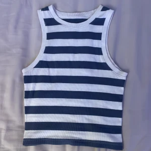 Randigt linne från Hollister - Säljer en fin randig linnetopp från Hollister i blått och vitt. Toppen är ribbad och ärmlös. Helt nytt skick, använd bara 1 gång! 