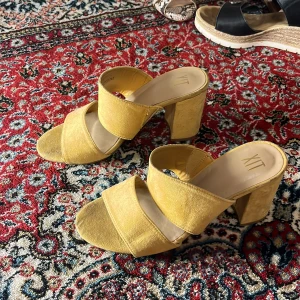 Gula sandaler med klack från XIT - Snygga gula sandaler med klack från XIT. Tillverkade i ett mjukt material med öppen tå och bred rem över foten. Perfekta för att liva upp din outfit med en färgklick.