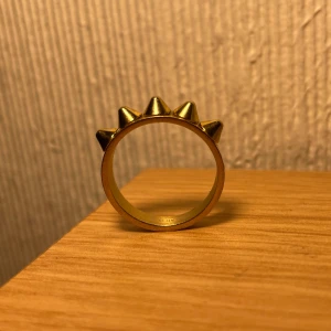 Guldfärgad ring med nitar - Snygg guldfärgad ring med spetsiga. Perfekt för att addera lite attityd till din stil. Köpte den till min flickvän men ringen var för stor. Köp båda ringarna för 300 kr. 