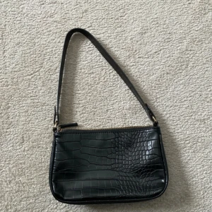 Svart axelväska med krokodilmönster - Snygg svart axelväska med krokodilmönster och dragkedja. Perfekt för en stilren look.
