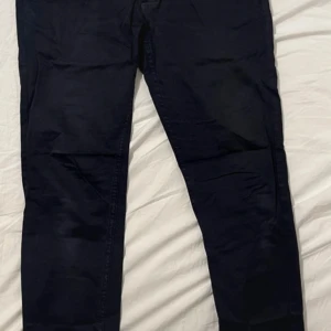 Svarta byxor med dragkedja och knapp - Snygga svarta byxor med dragkedja och knapp framtill. Perfekta för en stilren look. Byxorna har en klassisk design med bälteshällor och en diskret detalj vid midjan. Storlek EUR40