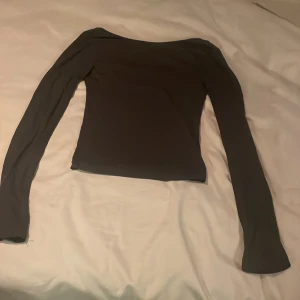 Grå långärmad topp, med öppen rygg. - Säljer en stilren grå långärmad topp med en elegant offshoulder-design. Perfekt för både vardag och festliga tillfällen. Toppen har en mjuk och bekväm passform.