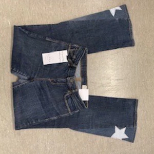 Blå jeans med stjärndetaljer - Snygga blå jeans med vita stjärnor på benen. De har en klassisk femficksdesign och en bekväm passform. Perfekta för en avslappnad stil. Köpta secondhand, omsydda av mined uf. 