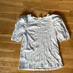 Ljusblåa t-shirt med puffärmar - Säljer en söt ljusblå inprincip oandvänd t-shirt med puffiga kortärmar. T-shortsen är i storlek S Perfekt för en stilren look. Blusen är i ett mjukt material och har en klassisk rund halsringning.