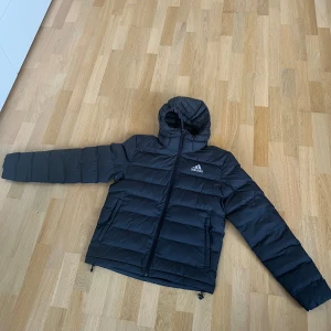 Svart dunjacka från Adidas - Har använt den här jackan när jag ska till kalla fotbolls matcher och den har funkat perfekt. Tyvärr så har jag vuxit ur den. Jackan har en klassisk pufferdesign med två fickor framtill.