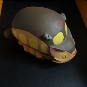 Sparbössa i form av en kattbuss - Charmig sparbössa formad som en kattbuss med bruna och gula detaljer. Den har små figurer på toppen och en öppning på undersidan för att ta ut pengar. Perfekt för fans av unika och lekfulla designobjekt.