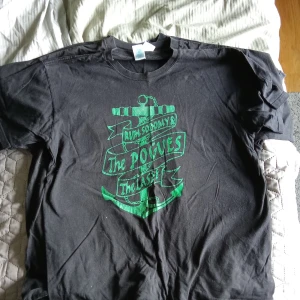 The pogues Svart t-shirt med tryck - Säljer en svart t-shirt med tryck i grönt och rött. T-shirten har ett ankarmotiv och texten 'Rum Sodomy & The Lash'. Perfekt för fans av the pogues
