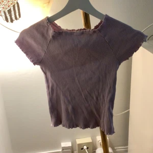 Lila ribbad topp från Lindex - Säljer en söt lila ribbad topp från Lindex. Toppen har korta ärmar och en fin vågig kant vid ärmslut och nederkant. Perfekt för en avslappnad stil.