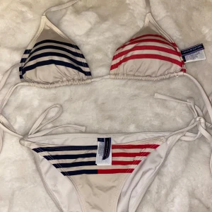 Randig bikini från Tommy Hilfiger - Snygg bikini från Tommy Hilfiger med triangelöverdel och knytband. Överdelen har randigt mönster i blått och rött, medan underdelen matchar med samma färger. Perfekt för sommarens stranddagar!