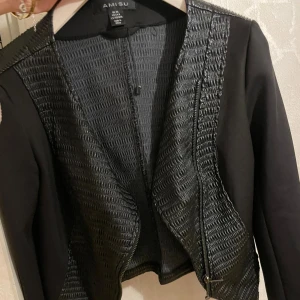 Svart jacka från Amisu - Snygg svart jacka från Amisu med unikt texturerat mönster framtill och på ryggen. Jackan har en asymmetrisk dragkedja och långa ärmar. Perfekt för att ge en stilren touch till din outfit.