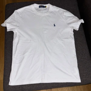 Vit t-shirt från Polo Ralph Lauren - Säljer en klassisk vit t-shirt från Polo Ralph Lauren med det ikoniska blå broderade logotypen på bröstet. T-shirten är kortärmad och tillverkad i mjuk bomull för en bekväm passform. Passar S/M, bara testad