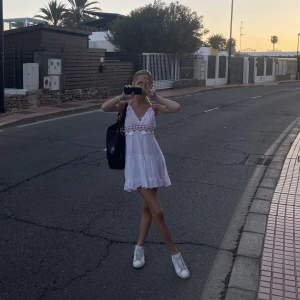 Vit sommarklänning med spetsdetaljer - Charmig vit klänning med v-ringning och spetsdetaljer. Perfekt för varma sommardagar. Klänningen är kort och har en luftig passform.