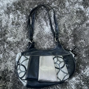Svart och grå axelväska med mönster - Snygg axelväska i svart och grått med unikt cirkelmönster. Väskan har dubbla axelremmar och en dragkedja för säker förvaring. Perfekt för att ge din outfit en stilfull touch.
