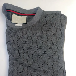 Grå tröja från Gucci - Säljer en stilren grå tröja från Gucci med det ikoniska GG-mönstret. Tröjan är tillverkad i Italien och har långa ärmar samt ribbade muddar. Perfekt för en lyxig och avslappnad look.
