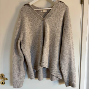 Grå stickad tröja med v-ringning - Mysig grå stickad tröja med v-ringning och långa ärmar. Perfekt för kyliga dagar med ribbade muddar vid ärmslut och nederkant. Enkelt och stilrent plagg för garderoben. Strl S men sitter mer som en M.