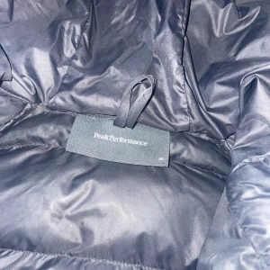 Svart dunjacka från Peak Performance - Jag säljer en mörklblå/svart jacka från Peak Performance med huva och dragkedja. Jackan är perfekt för kalla dagar och har en stilren design med quiltade detaljer. Den är långärmad och passar bra för vinter och höst. Jackan är välanvänd men ändå bra skick förutom att den har två hål i armen!