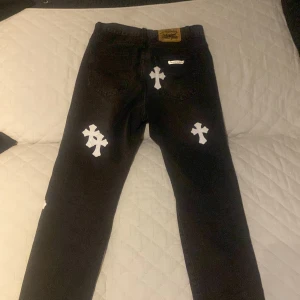 Svarta jeans med vita korsdetaljer - Snygga svarta jeans med unika vita korsdetaljer. Perfekt för dig som vill sticka ut med en edgy stil. Jeansen har en klassisk passform och är tillverkade i ett slitstarkt material.