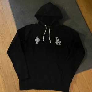 Svart hoodie från Marcelo Burlon - Säljer en svart hoodie från Marcelo Burlon med LA-logga på bröstet och ryggen. Perfekt för en avslappnad stil. En väldigt sällsynt modell som få äger