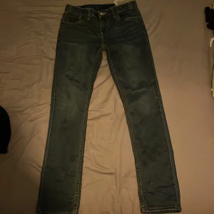 Blå jeansbyxor från Levi's - Snygga blå jeansbyxor från Levi's med klassisk femficksdesign och knappgylf. Perfekta för en avslappnad stil. Levi's logotyp syns på baksidan. Folk som är upp till ca 173 kan ha dessa jeans och dom är sköna i midjan och härliga på längden.