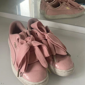 Rosa sneakers från Puma - Säljer ett par rosa Puma sneakers med breda snören och en glansig finish. Skorna har en klassisk design med Pumas logga i guld på sidan. Dom är perfekta för sommaren 🌷💓