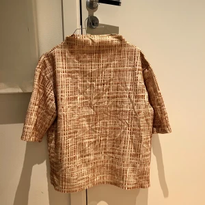 Fin topp med struktur - Säljer en unik beige topp från KappAhl med ett coolt mönster i brunt. Toppen har trekvartsärm och en avslappnad passform. 
